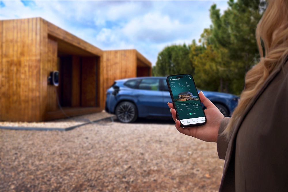 รถ BMW Neue Klasse จอดชาร์จหน้าบ้านไม้พร้อมหน้าจอแอปจัดการพลังงานบนสมาร์ทโฟน
