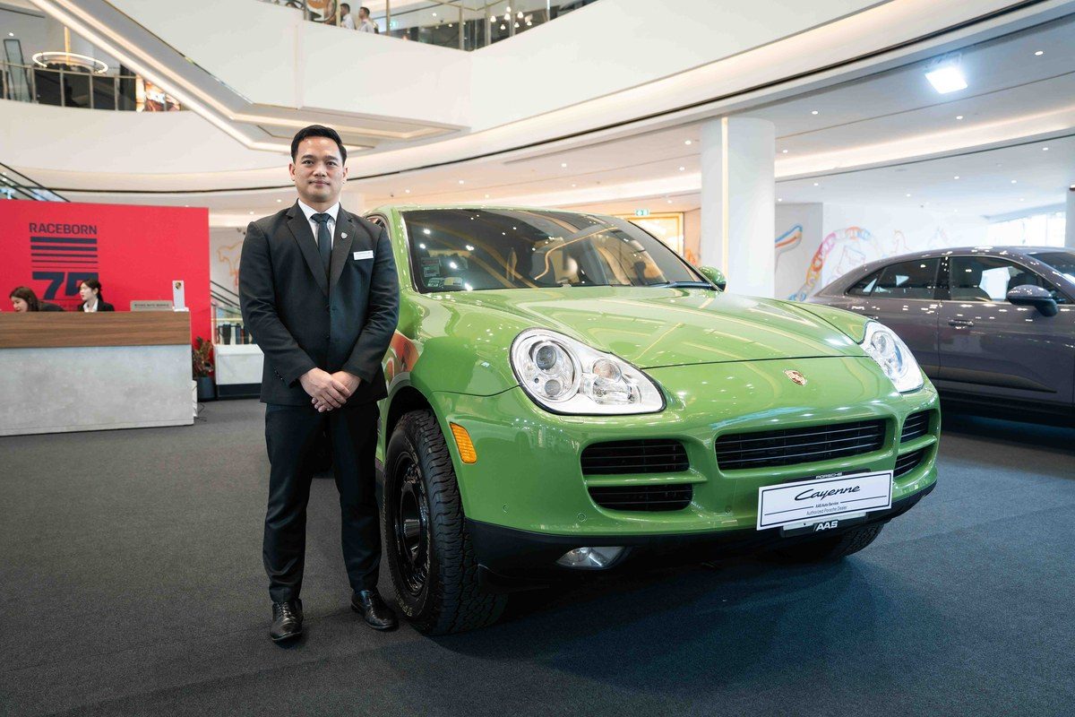 ภาพรถยนต์ Porsche Cayenne สีเขียวตั้งอยู่ในงานเปิดตัวพร้อมกับผู้บริหารที่ยืนอยู่ข้างๆ.