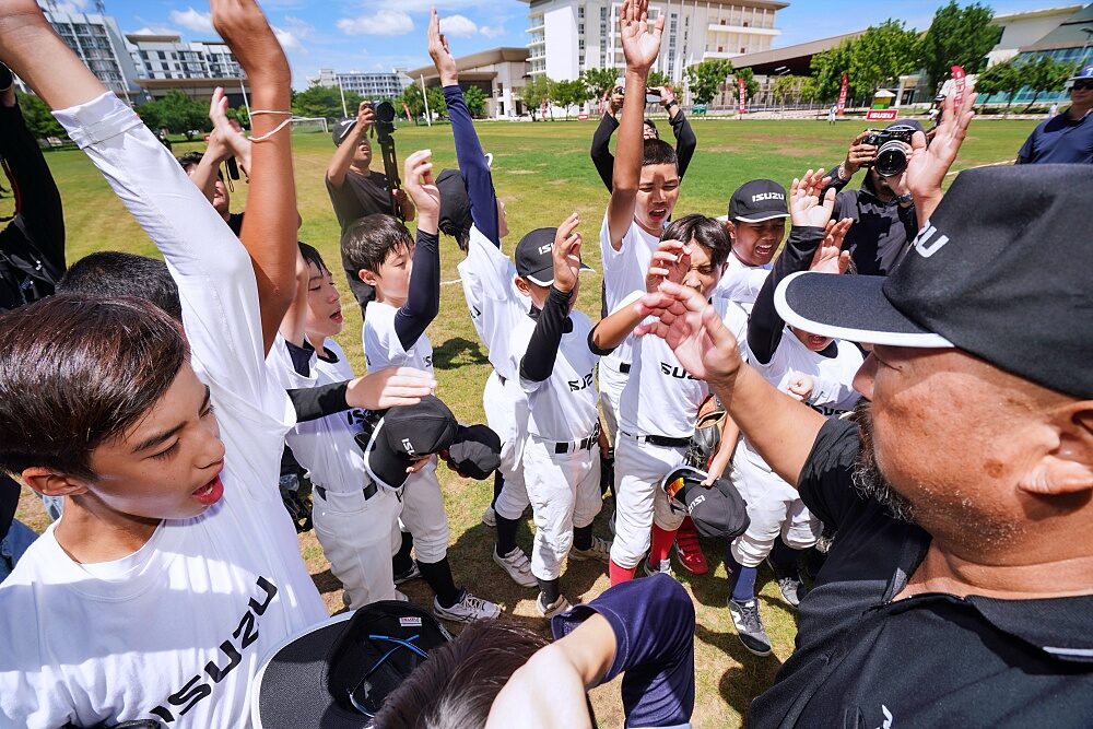 Youth baseball players raise hands together with coaches