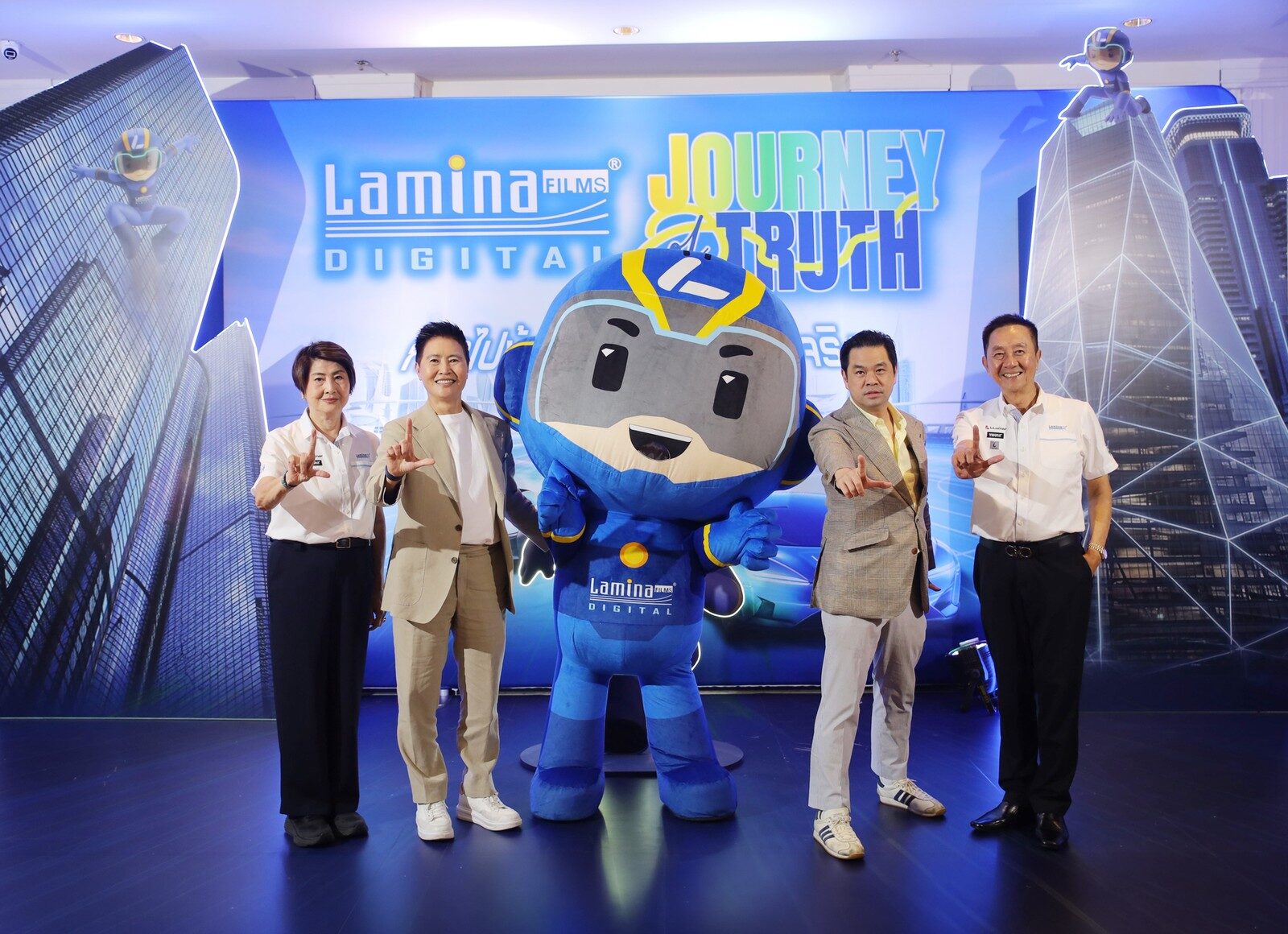 ผู้บริหารยืนข้างมาสคอตหน้าฉาก Lamina Journey of Truth
