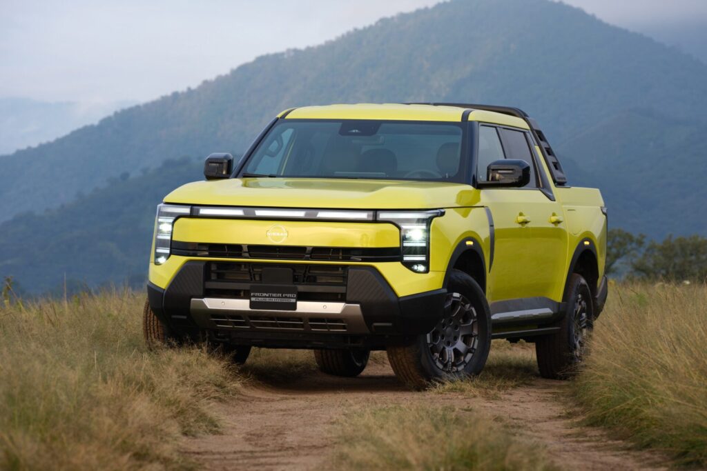Nissan Frontier Pro PHEV สีเหลืองมุมหน้าเฉียงบนทางดินกลางทุ่งหญ้า