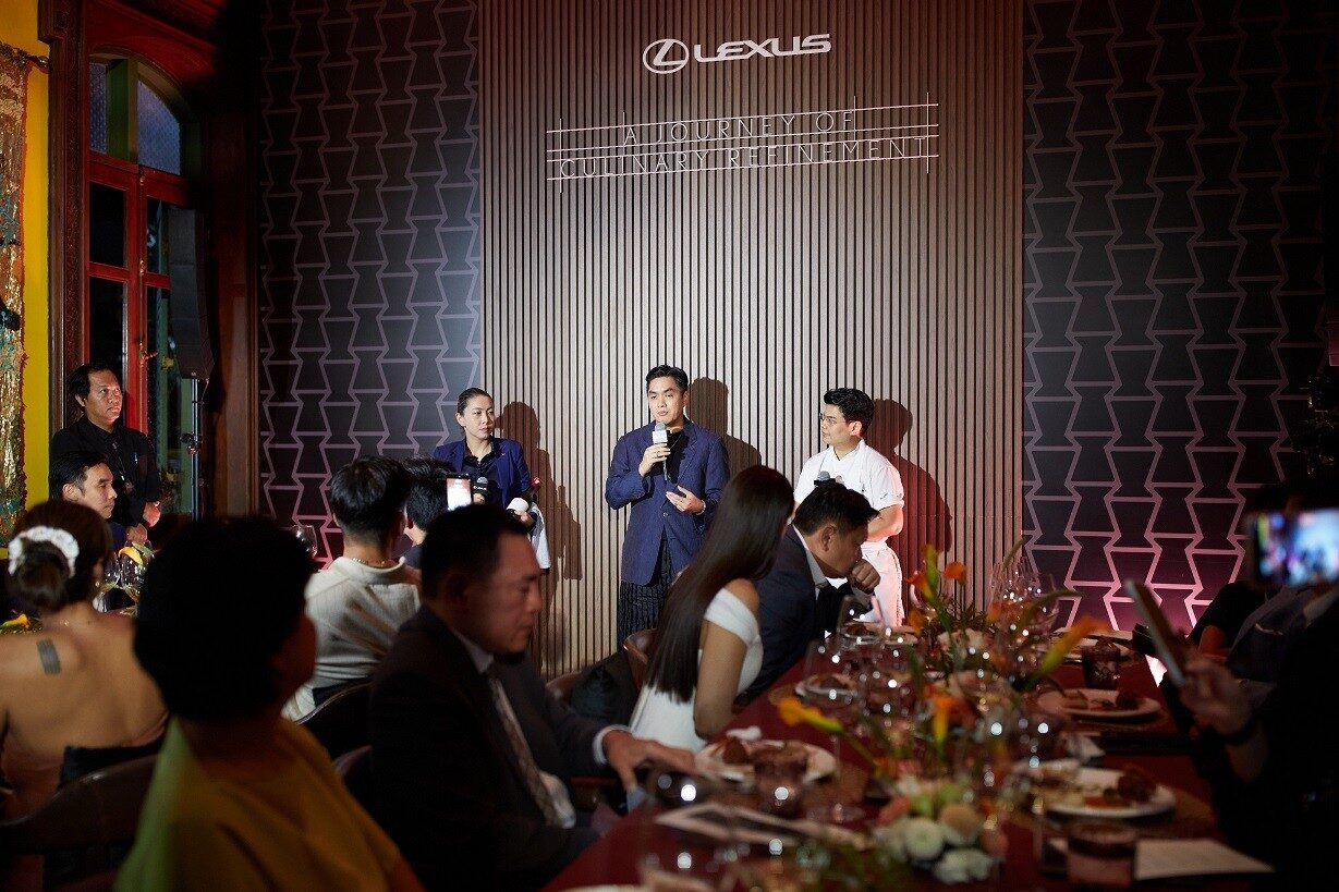 เวทีกิจกรรมมีโลโก้ Lexus เป็นฉากหลัง มีผู้ร่วมงานนั่งโต๊ะอาหารด้านหน้า