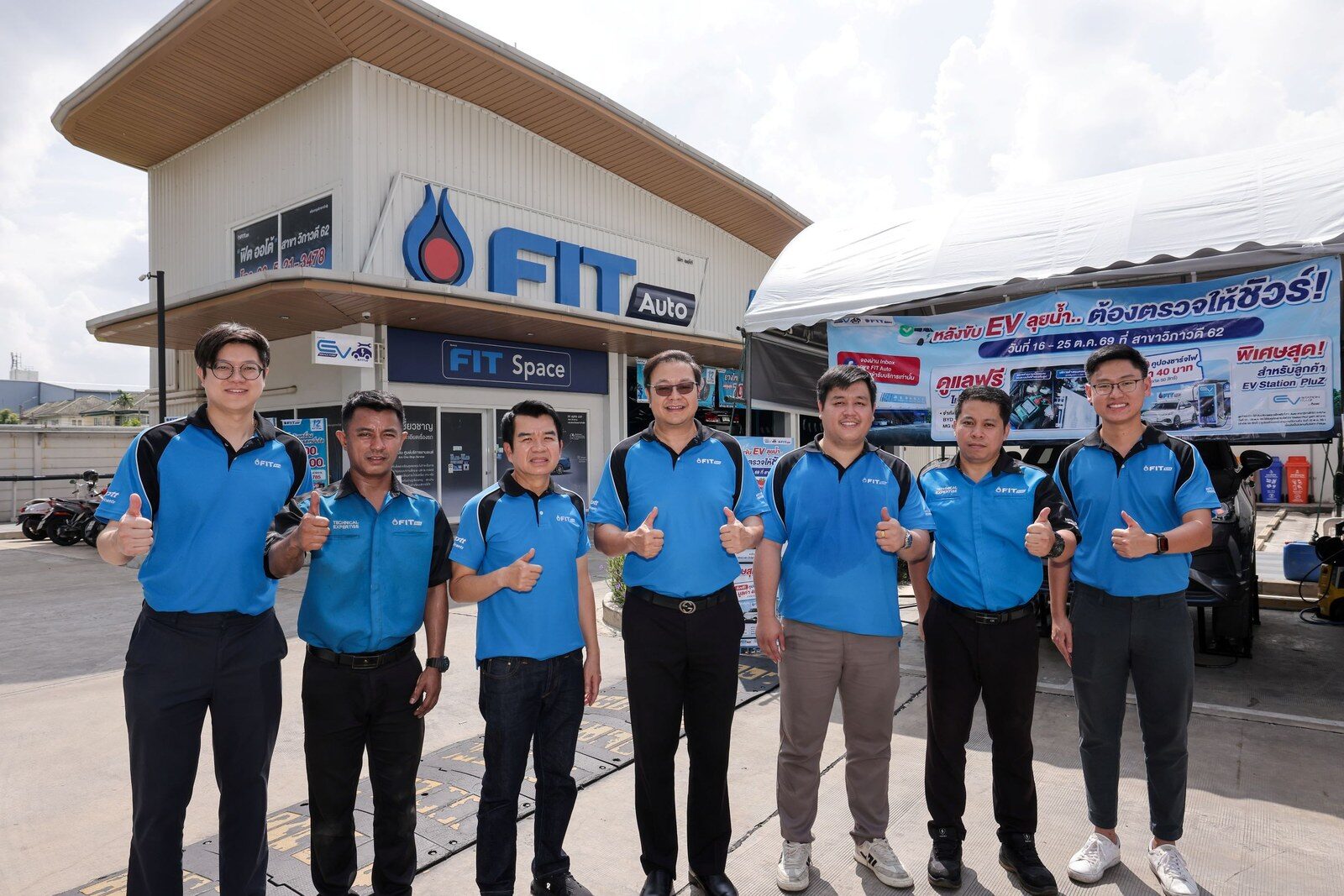 ทีมงานในชุดพนักงาน FIT Auto 7 คนยืนชูนิ้วโป้งหน้าศูนย์บริการ