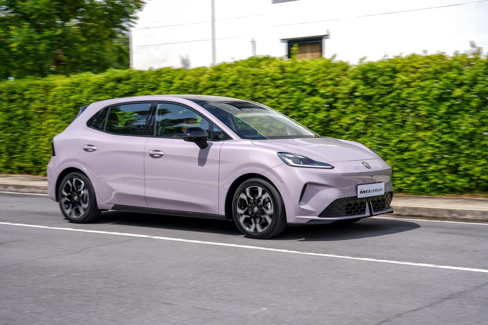 MG Urban สีม่วงพาสเทลขณะแล่นบนถนน มองเห็นด้านหน้าและด้านข้างตัวรถ