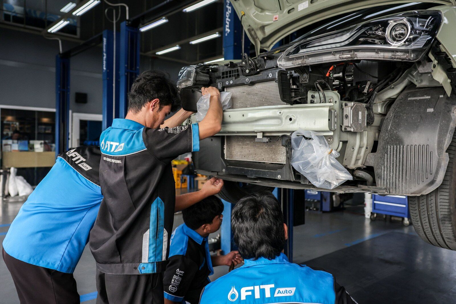 ช่าง FIT Auto ตรวจดูบริเวณด้านหน้ารถที่เปิดฝากระโปรงบนลิฟต์ยก