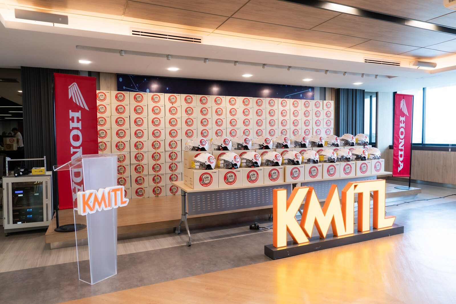 บรรยากาศเวทีงานส่งมอบ กองกล่องและหมวกกันน็อก ป้าย KMITL และธงฮอนด้า