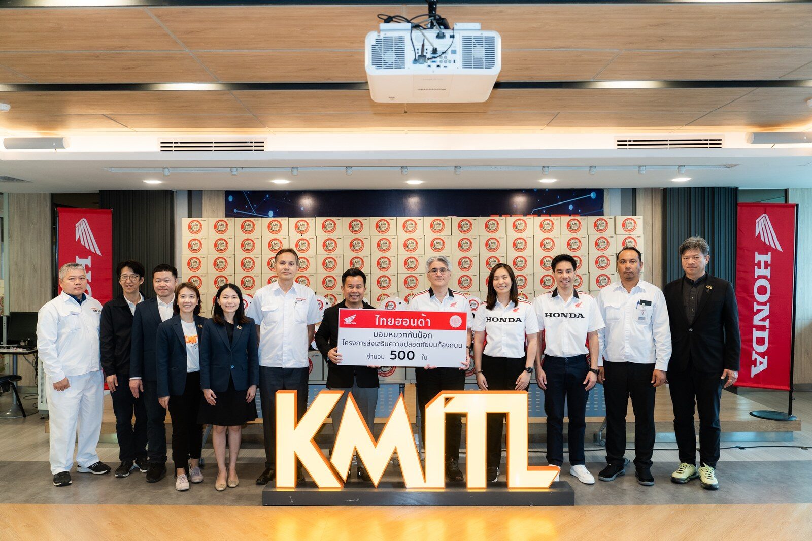 ผู้บริหารไทยฮอนด้าและคณะผู้บริหาร สจล. ยืนถือป้ายส่งมอบหมวกกันน็อก 500 ใบ