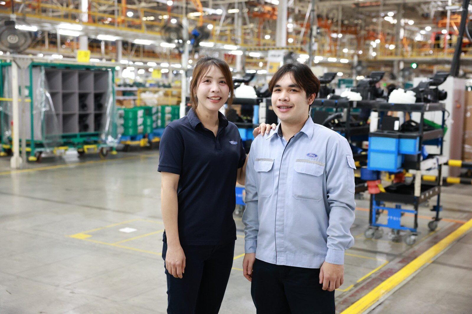 พนักงานหญิงชุดโปโลสีกรมท่ายืนคู่กับช่างเทคนิคชายในโรงงานฟอร์ด
