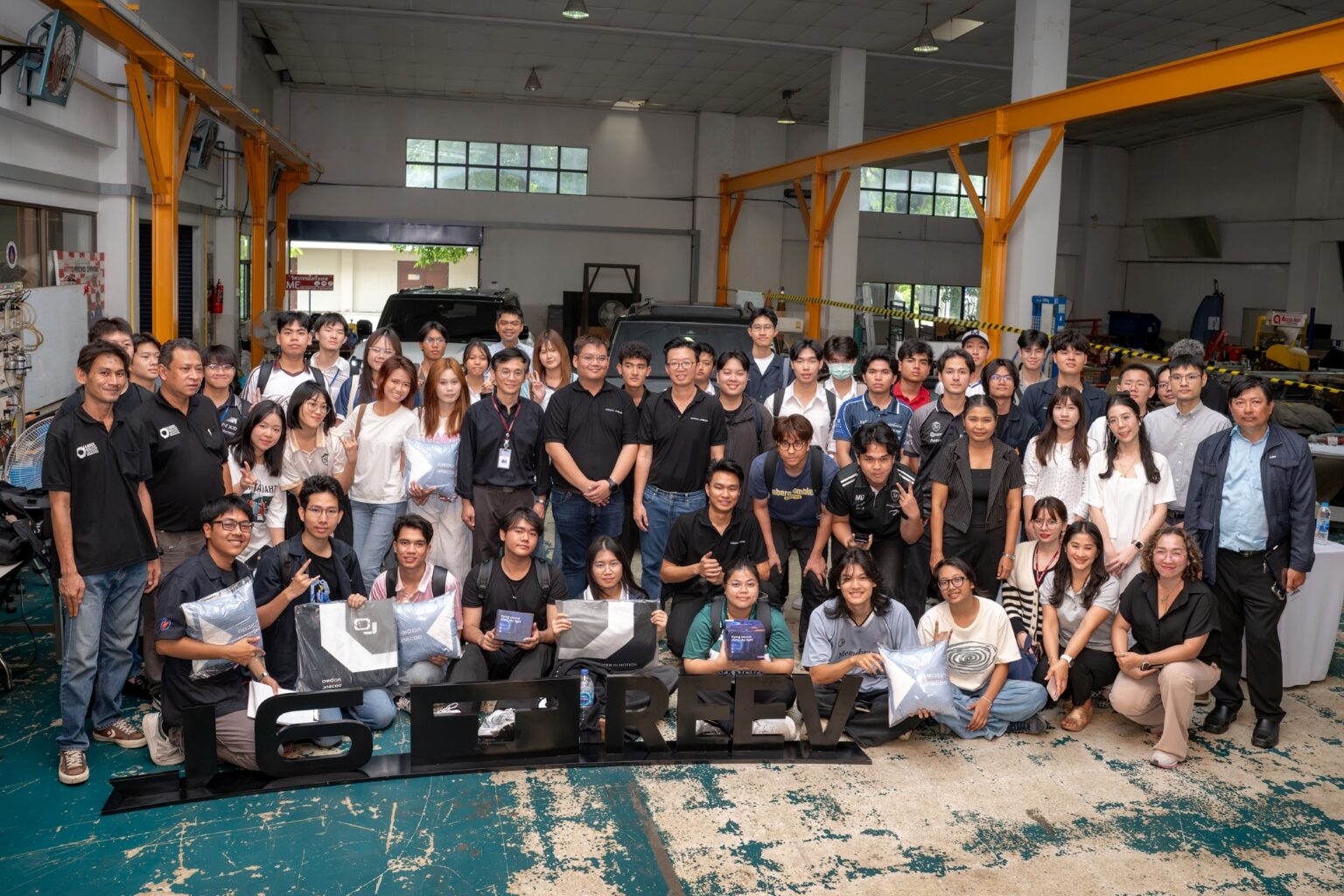 ภาพหมู่นักศึกษาและทีมงานในโรงปฏิบัติการ มีป้าย J6T REEV วางด้านหน้า