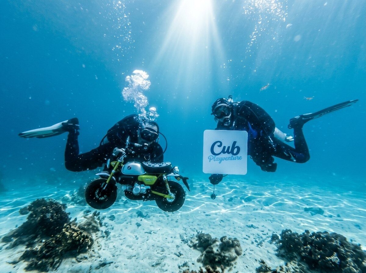 นักดำน้ำสองคนกับรถ Honda Monkey และป้าย Cub Playventure ใต้ทะเล