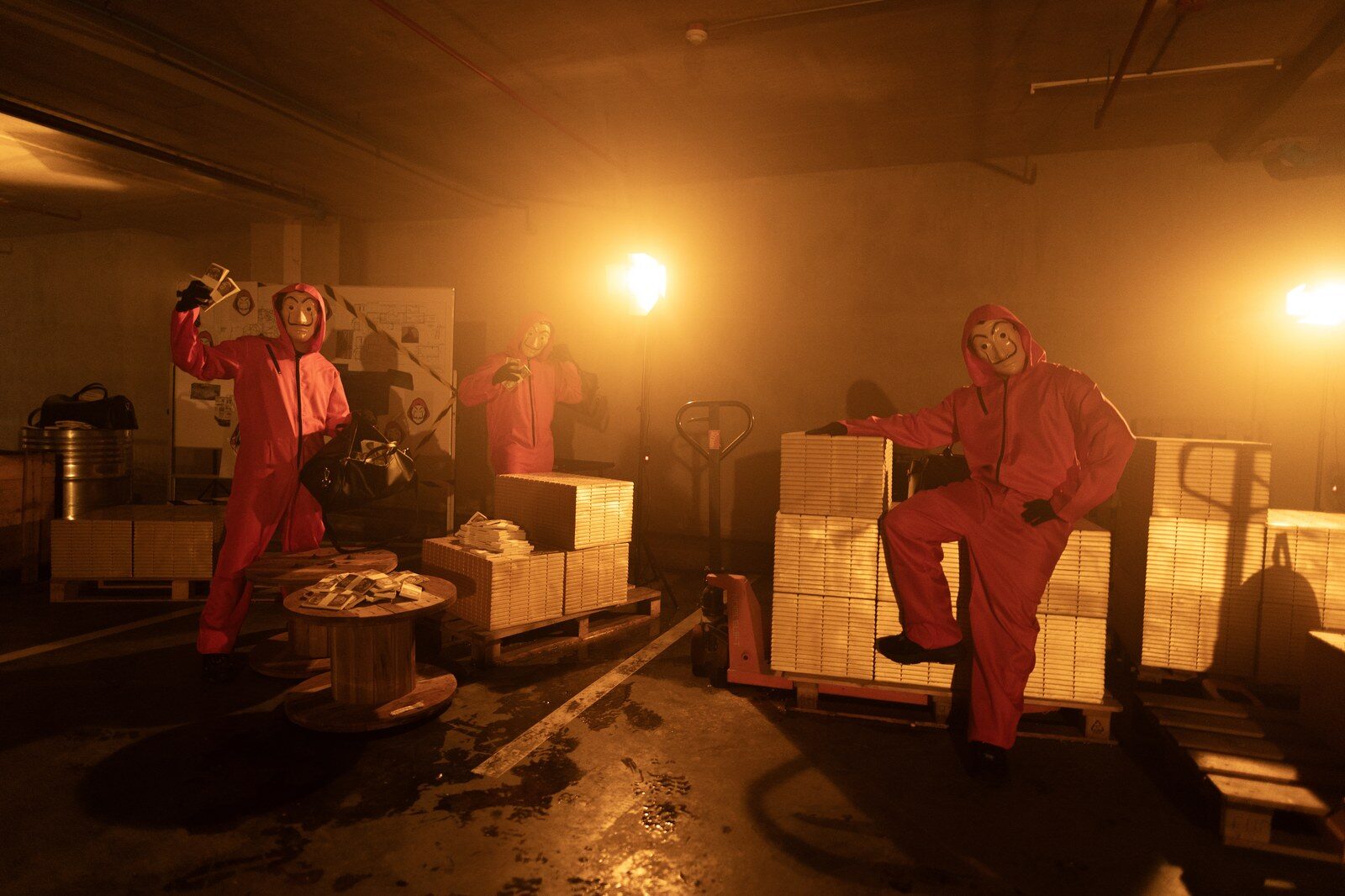 ผู้สวมชุดแดงและหน้ากากยืนอยู่กับกองแท่งทองจำลองบนพาเลทในฉากธีม Money Heist