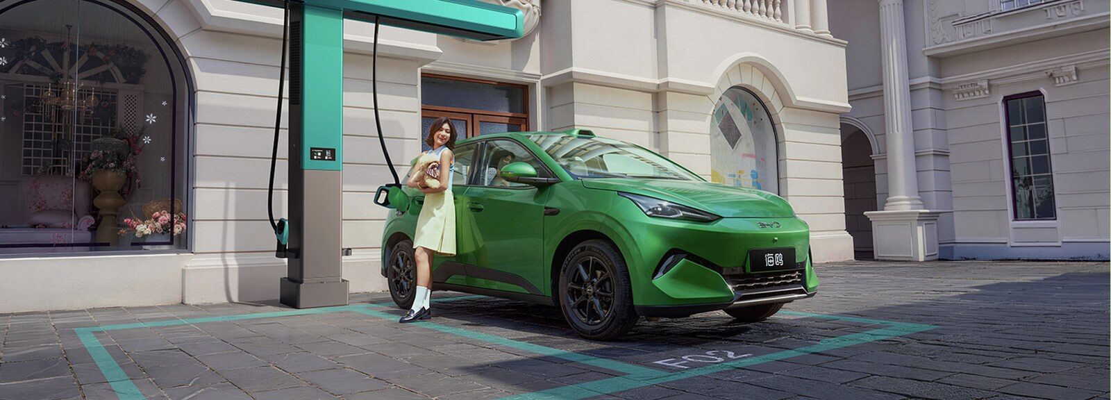 BYD Seagull เจน 2 สีเขียว จอดที่ตู้ชาร์จแฟลช มีผู้หญิงอุ้มสุนัขยืนข้างรถ