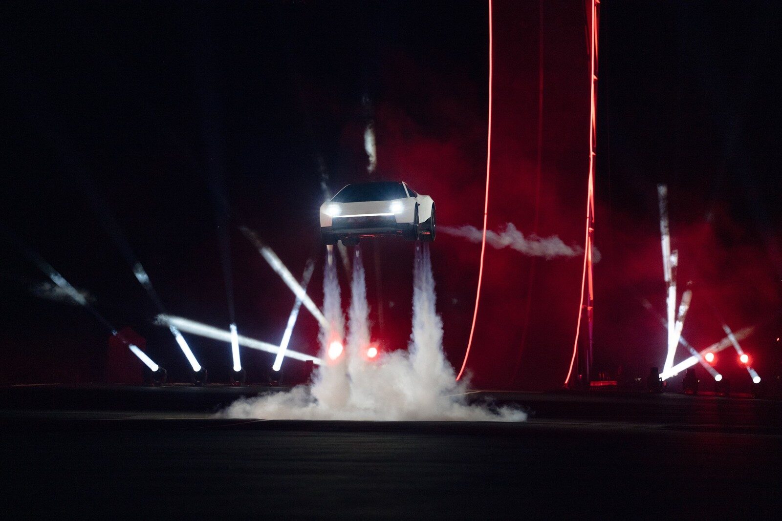 Roadster สีขาวลอยกลางอากาศพร้อมไอพ่นจากด้านล่างบนเวทีมืด